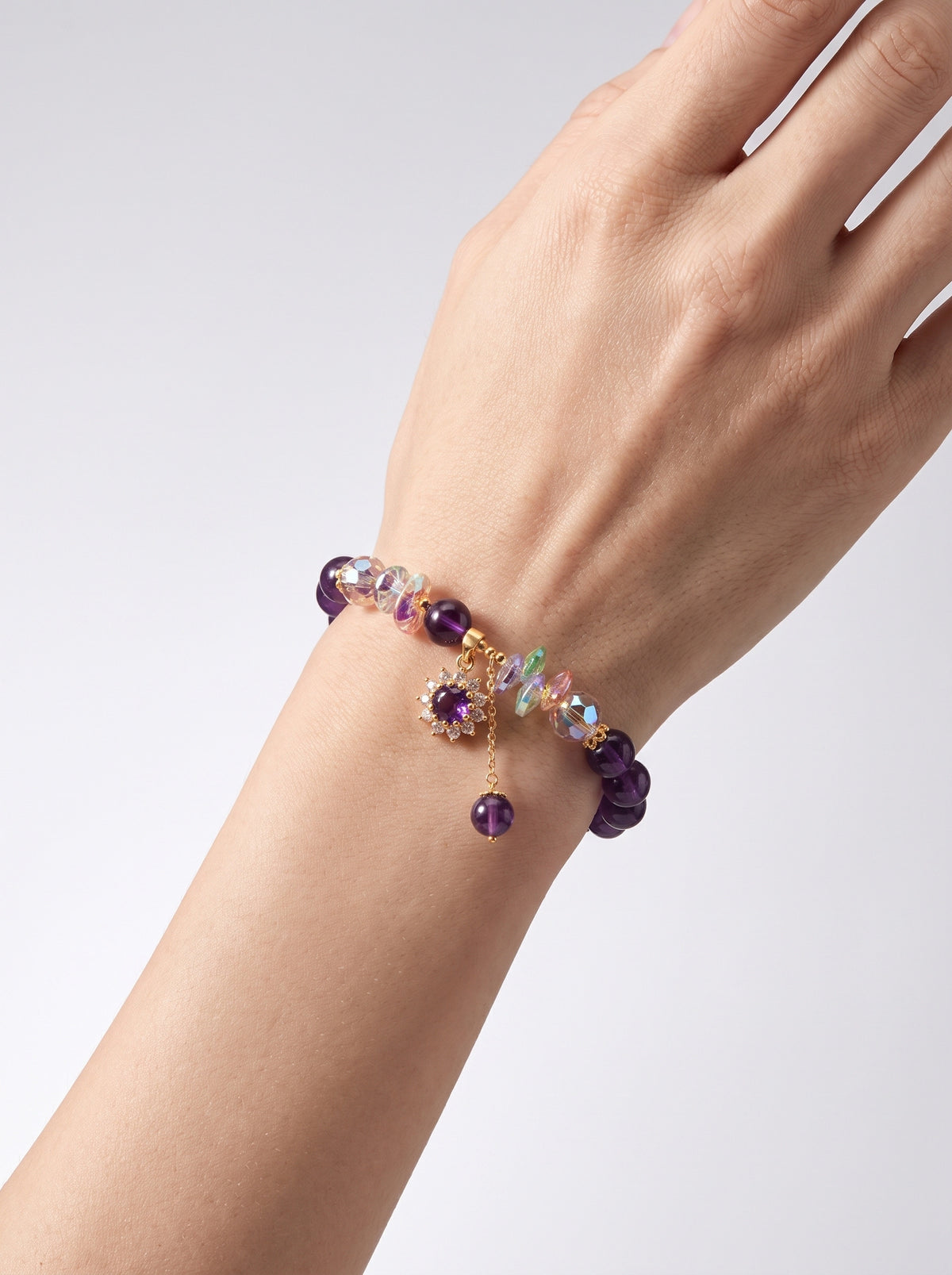 Amethyst bracelet worn on a wrist, showing the purple flower charm and dangling bead against a light background.
